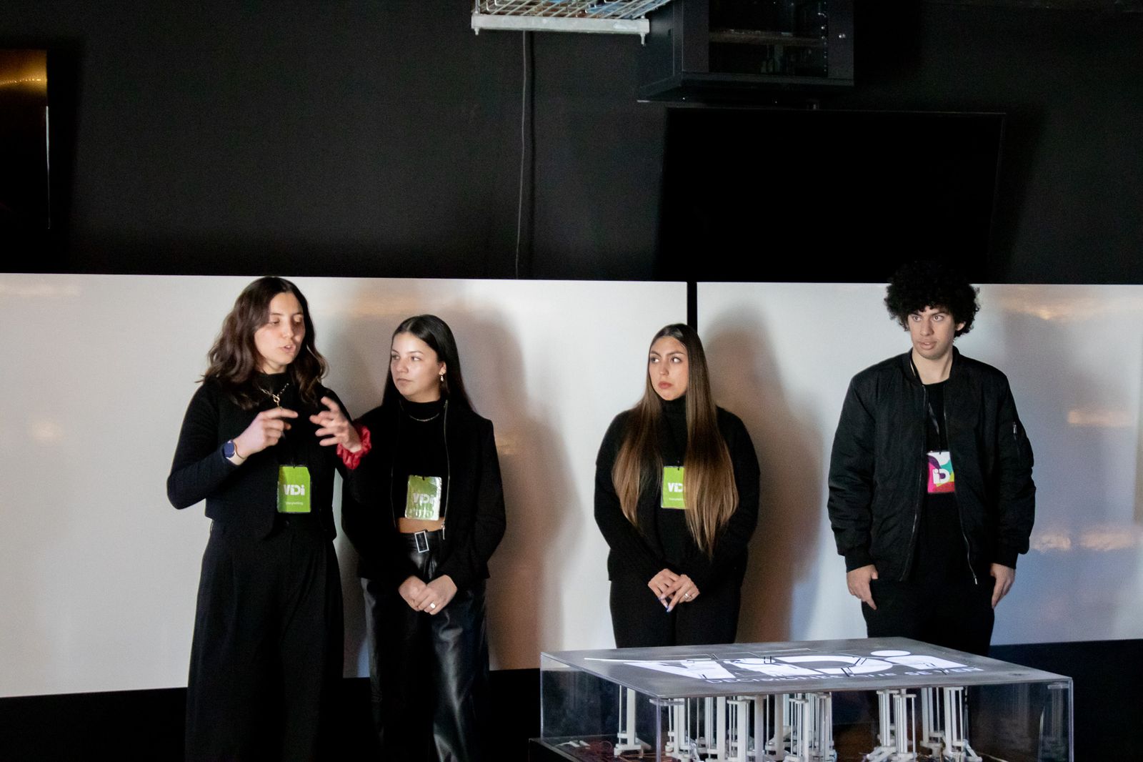 Four presenters standing in front of the white wall, one speaking